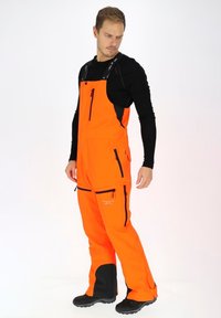Heldere oranje waterdichte overalls met zwarte accenten, verstelbare banden, meerdere ritszakken en verstevigde onderbenen voor duurzaamheid.