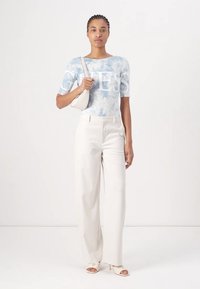 Top corto a maniche corte in tie-dye azzurro chiaro con grande lettering bianco, abbinato a pantaloni bianchi a vita alta e sandali con tacco color nude.