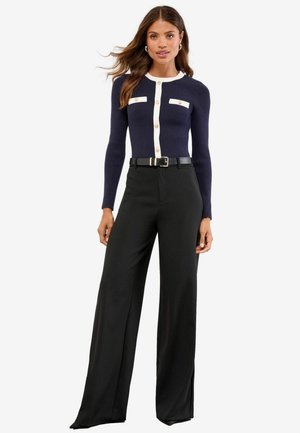 Navy ribbed cardigan with white accents and buttons, paired with black high-waisted, wide-leg trousers and a black belt.