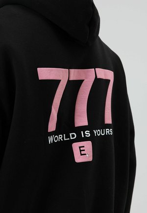 Schwarzer Hoodie mit großem pinkfarbenem "777"-Aufdruck auf dem Rücken, darunter "WORLD IS YOURS" in Weiß und ein kleines pinkfarbenes Quadrat mit einem "E". Mit strukturiertem Akzent.