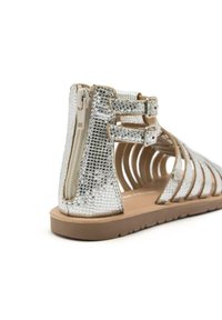 Sandales argentées avec un motif texturé reptilien. Comprend deux sangles à boucles réglables et une fermeture éclair sur le côté. Semelle plate avec un design ouvert.