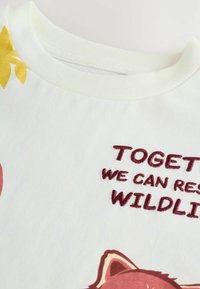Camiseta de algodón blanca con cuello redondo, diseño floral amarillo y texto bordado en marrón "JUNTOS PODEMOS SALVAR LA FAUNA" con una ilustración de un zorro.