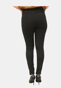 Jeans skinny neri con vita alta, dotati di due tasche posteriori e una texture liscia. Indossati con scarpe con tacco nero.