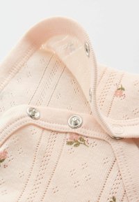 Mjuk rosa stickad tyg med små blommönster och silverfärgade tryckknappar på kanten av ett babyplagg.