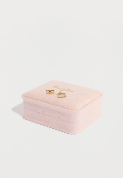 Scatola per gioielli in velluto rosa con dettagli in oro, contenente orecchini geometrici. La scatola presenta una texture morbida e un logo dorato sul coperchio.