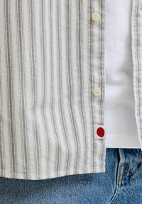 Rövid ujjú, gombos ing vízszintes fehér és fekete csíkokkal, piros díszítéssel az oldalán és krémszínű gombokkal.