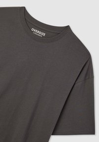 Oversize ciemnoszary t-shirt wykonany z miękkiej bawełny. Posiada okrągły dekolt i krótkie rękawy, z minimalną liczbą szwów i gładką fakturą.