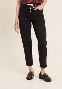 Schwarze Hosen mit lockerer Passform, ausgestattet mit zwei vorderen Taschen und einem Kordelzugbund. Umschlagabschlüsse und eine glatte Stofftextur sorgen für Details.
