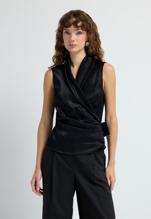 Musta satiininen hihaton toppi, jossa on kietaisusuunnittelu, sivusolmu, sileä tekstuuri ja hieman kaareva helma. Yhdistetty mustiin housuihin.