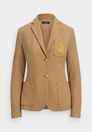 Sacou de culoare cămilă, cu un material texturat, cu rever în formă de clopot, două nasturi aurii și un logo decorativ brodat în aur pe buzunarul de la piept.