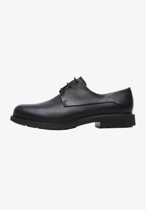 Zapato de vestir de cuero negro para hombre con tres ojales, punta redondeada y suela de goma gruesa visto desde el lado exterior.