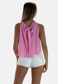 Blusa sin mangas de color rosa con un escote fruncido y un lazo atado en la parte de atrás. Combinada con pantalones cortos de mezclilla blancos con el dobladillo deshilachado.
