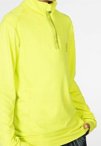 Sudadera de manga larga de color amarillo brillante con cuello alto, cierre de media cremallera en la parte delantera y un logotipo sutil. Textura suave y diseño ajustado.