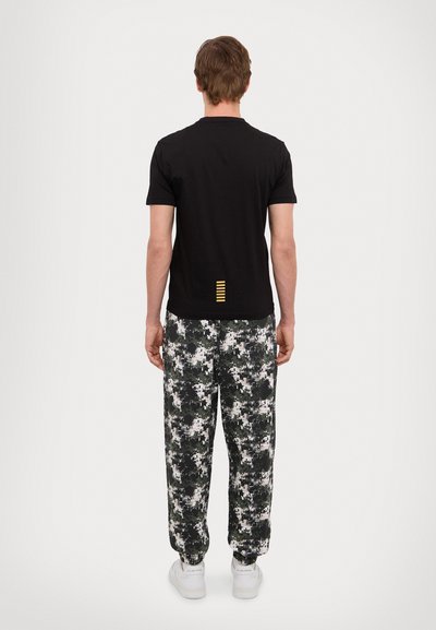 T-shirt noir en coton à manches courtes, doté d'un détail rayé jaune au dos ; associé à un pantalon ample à motif camouflage.