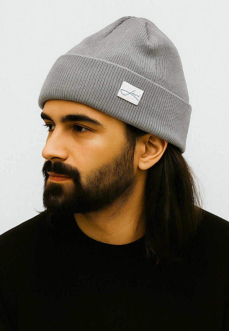 Gray knitted beanie with a ribbed texture, featuring a small white tag with blue lettering. The design is fitted and simple.