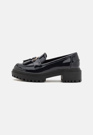 Marineblå patentlæder loafers med frynser, guldfarvet hardware og chunky sort gummisål med lugs design, skrå vinkel fra siden.