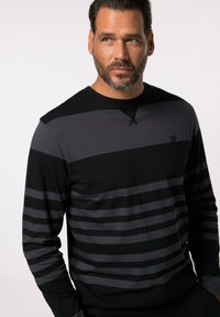 Chemise à manches longues avec des rayures horizontales noires et gris foncé, un col rond et un logo discret sur la poitrine. Fabriquée en tissu doux.