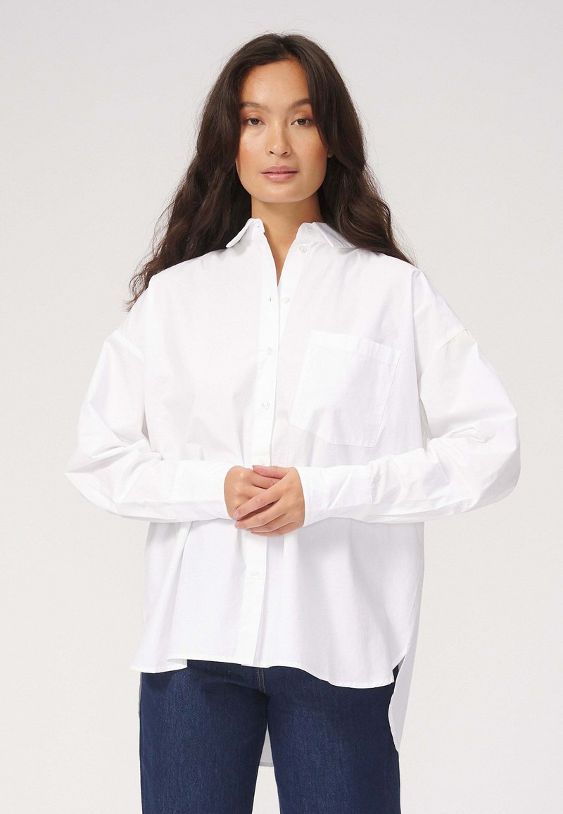 Hvid skjorte med lange ærmer, enkelt brystlomme og en afslappet pasform. Fremstillet af glat stof med en let struktureret overflade.