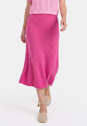 Donna che indossa una gonna midi rosa acceso con piccoli scintillii, un top in maglia rosa e espadrillas beige con lacci alla caviglia.