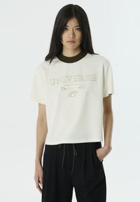 Korte mouwen crème t-shirt met een bruine geribbelde kraag, met geborduurde "UNIVERSE" tekst en een planetenafbeelding op de voorkant. Gladde textuur.