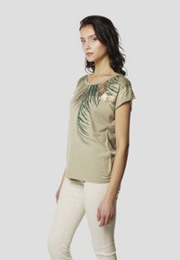 Gaiši zaļa īsroku T-krekls ar palmā lukturas grafiku tumši zaļā un zelta krāsā, ar apaļu kakla izgriezumu un mīkstu audumu.