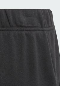 Pantalons de survêtement noirs avec une taille élastique texturée, un fin côtes et un fini en tissu doux et lisse. Pas de logos ni de motifs visibles.