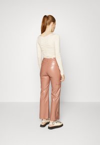 Top de manga longa, creme, com detalhe nas costas franzido, combinado com calças cargo rosadas de pele sintética de cintura alta, apresentando fendas laterais e bolsos.
