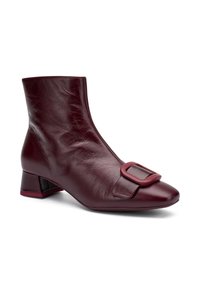 Botín de cuero burdeos hasta el tobillo con punta cuadrada, que presenta un detalle de hebilla lateral y un tacón bajo y cuadrado. Textura suave con un ligero brillo.