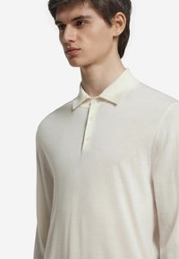 Långärmad polo i krämfärg med en mjuk textur, krage, tre knappar och en ren, enkel design.