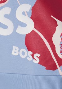 Felpa blu con grande scritta bianca "BOSS", design floreale rosso e orlo a coste. Texture liscia con dettagli di stampa ben definiti.