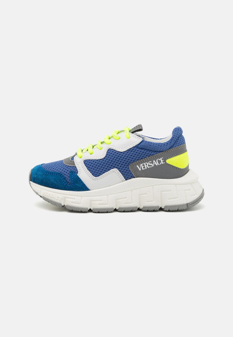 Kék és fehér hálós sportcipő velúr részletekkel, világító sárga fűzőkkel, vastag, texturált talppal és egy szürke panellel, amelyen a "VERSACE" márkázás látható.