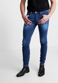 Dunne blauwe jeans met een vervaagd detail op de dijen, voorzien van een klassiek vijf-pocket ontwerp en gecombineerd met zwarte enkellaarsjes.