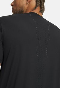 Camiseta deportiva negra con textura suave, mangas cortas y una fila vertical de pequeños perforaciones en la espalda para ventilación.
