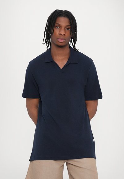 Camisa polo de color marino con cuello y mangas cortas, hecha de una tela texturizada. Dobladillo recto con una pequeña etiqueta de logo en el lateral.