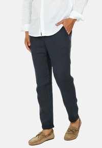 Pantaloni in lino blu navy con vestibilità affusolata, tasche laterali e una finitura testurizzata, abbinati a scarpe mocassino color marrone chiaro.