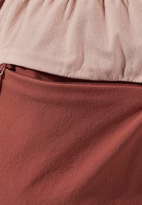 Lichtroze top met geplooide textuur ontmoet een roestkleurige onderkant, met een gladde textuur en een zichtbare rits langs de naad.