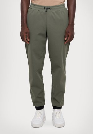 Olive green, lightweight joggers with adjustable drawstring waist, tapered legs, and black cuffs at ankles, paired with white sneakers.