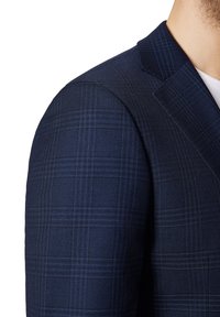 Granatowa marynarka w kratę z teksturowanej tkaniny, z niebieskimi akcentami w wzorze. Szczegółowo wykończony kołnierz i wyraźnie zarysowane ramiona.