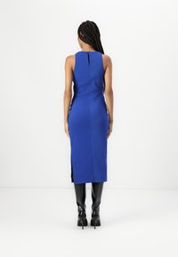 Blå ärmlös klänning med hög halsringning, figursydd design, sprund på sidan och detalj med nyckelhål på baksidan. Matchad med svarta knähöga stövlar.