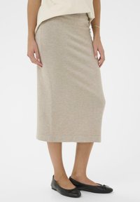 Béžová pletená sukně po kolena s přiléhavým střihem a jemnou žebrovanou texturou, doplněná černými balerínami s mašlí.