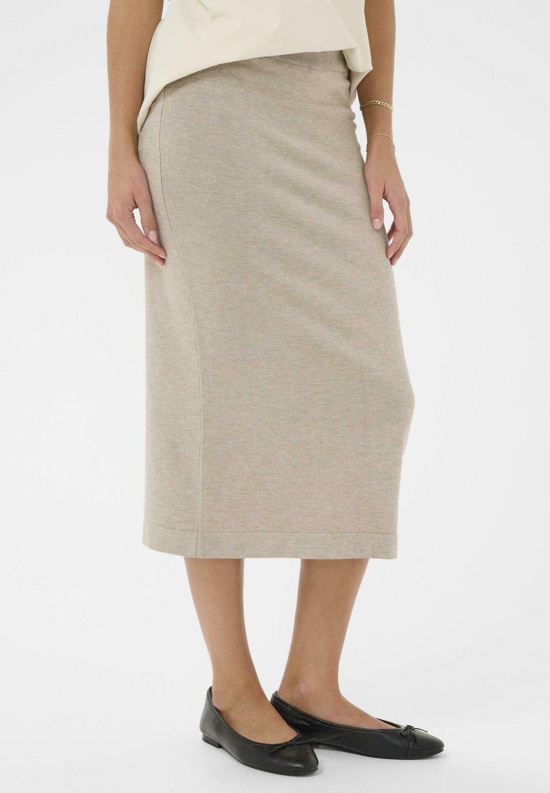 Béžová pletená sukně po kolena s přiléhavým střihem a jemnou žebrovanou texturou, doplněná černými balerínami s mašlí.