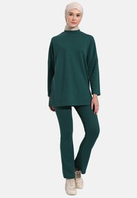 Green two-piece outfit featuring a long, loose-fitting top with a mock neck and matching slim-fit pants, made of textured fabric.