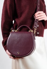 Bordowa skórzana torebka o zaokrąglonym, ustrukturyzowanym kształcie. Posiada górny uchwyt, regulowany pasek oraz złote elementy ozdobne.