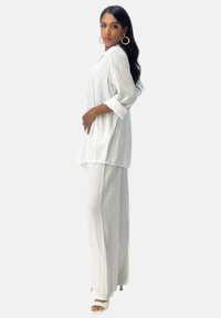 Weiße Tunika mit Textur und passenden weit geschnittenen Hosen, aus leichtem Stoff gefertigt. Verfügt über umgeschlagene Ärmel und ein minimalistisches Design.