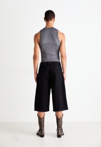 Gray sleeveless top, loose black knee-length shorts, and detailed brown cowboy boots. Smooth fabric with a subtle sheen.