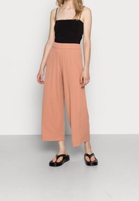 Pantalons larges plissés rose clair avec une taille élastique, associés à un débardeur noir et des sandales à plateforme noires.