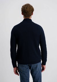 Marineblauwe gebreide trui met hoge kraag, textuurpatroon en geribbelde manchetten; gecombineerd met lichtblauwe denim jeans.