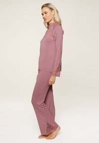Ensemble de vêtements d'intérieur dans un mauve doux, comprenant des manches longues et des accents en dentelle sur les épaules et les ourlets des pantalons. Tissu doux et confortable avec une coupe décontractée.
