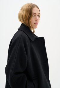 Zwarte wollen jas met een gestructureerde kraag, oversized pasvorm en zijzakken, met een soepele textuur en minimalistisch ontwerp.