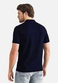 Marineblauwe polo van korte mouwen, met een klassieke kraag en een gladde textuur, gecombineerd met lichtblauwe spijkerbroek.